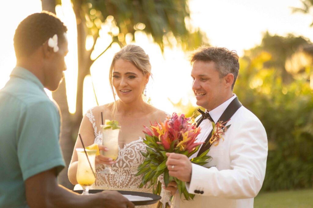Kylee & Jason at Outrigger Fiji Beach Resort - images by Ocean Studio Fiji - bride and groom holding flowers with resort staff